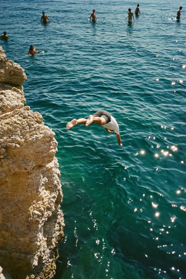 A man dives off a rocky cliff into turquoise water