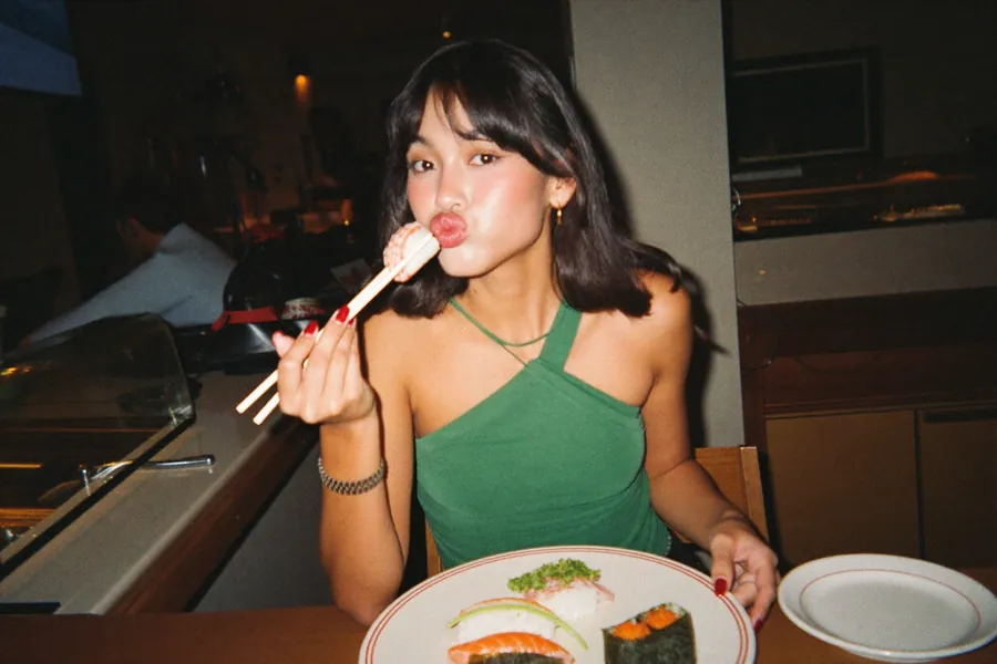A woman in a green top mid-bite at a sushi counter