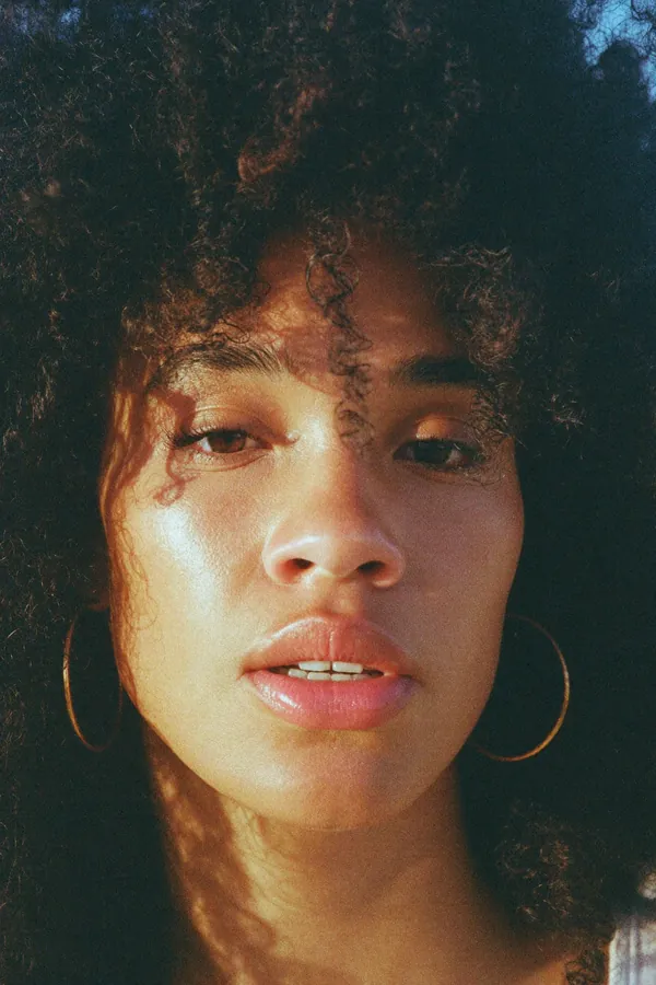 Close-up of a woman with curly hair and a tear on her cheek in golden light